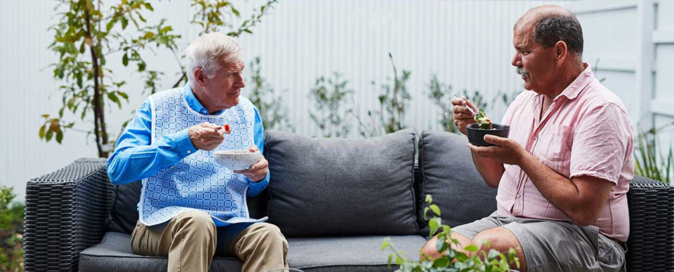 two elderly man wearing adults bibs siting outdoor