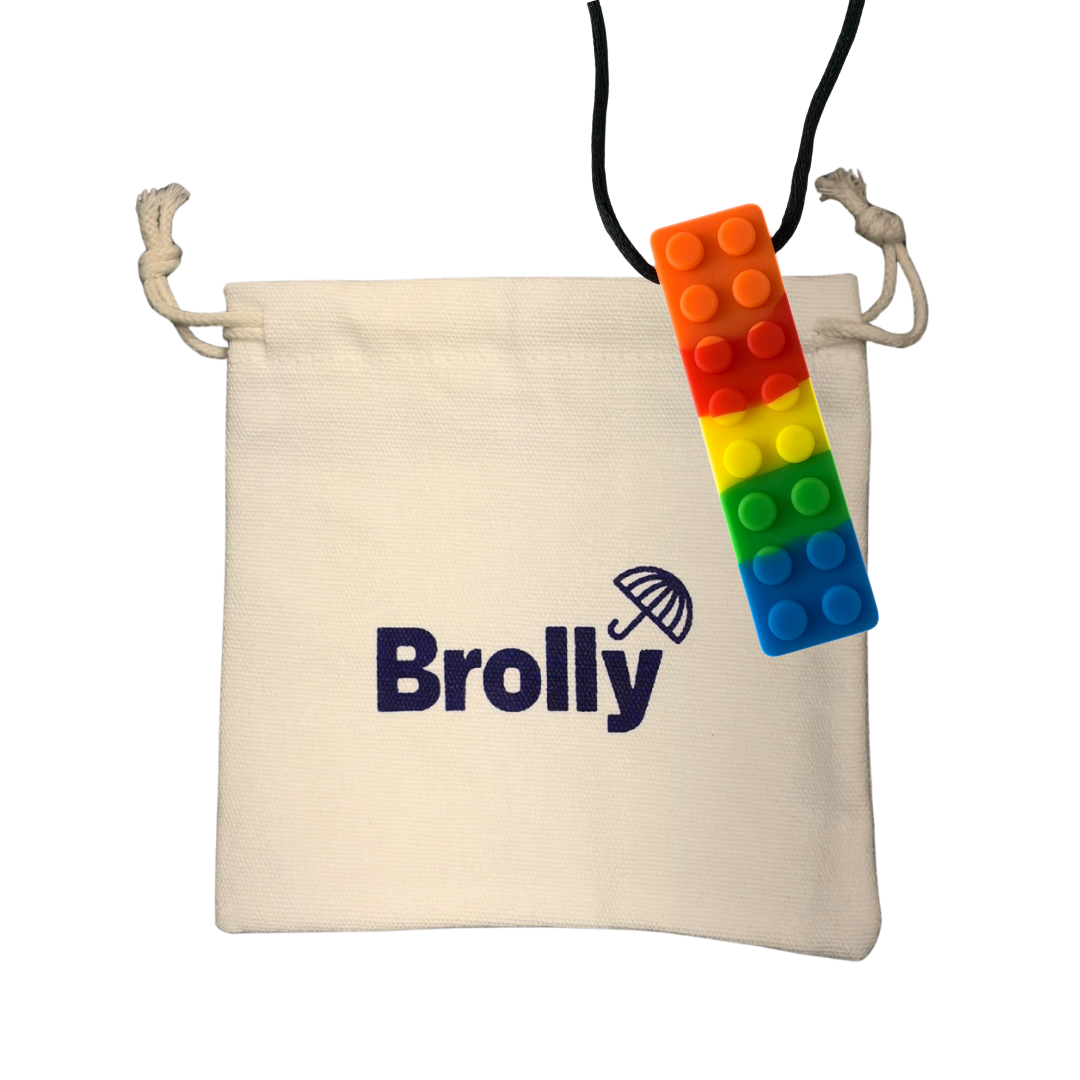 Beige drawstring pouch and Rainbow brick-shaped Brolly Chew Necklace on a black cord against a white background - Rainbow