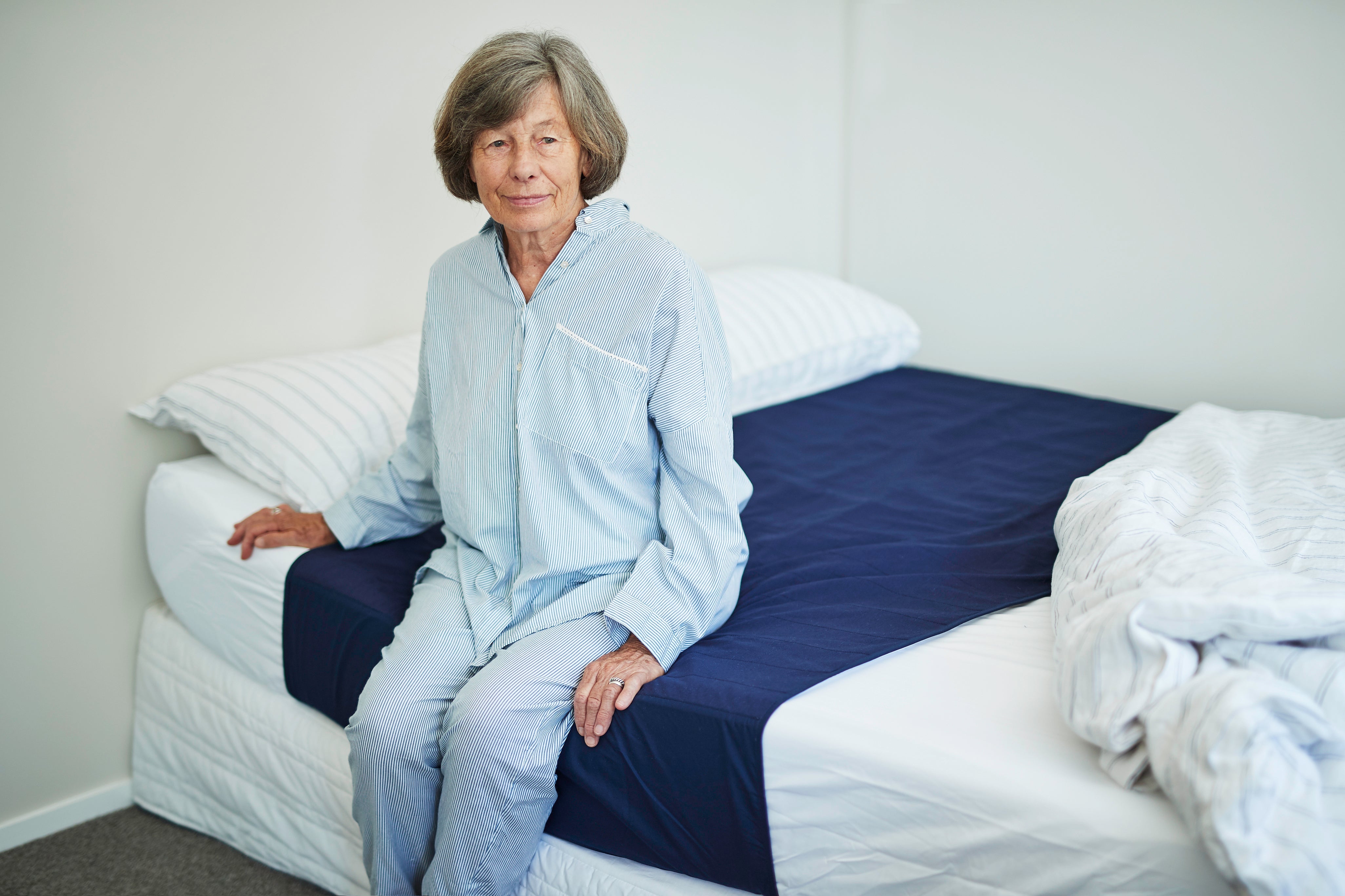 An elderly woman relaxes on a bed in a cozy room, surrounded by soft lighting and personal items. 