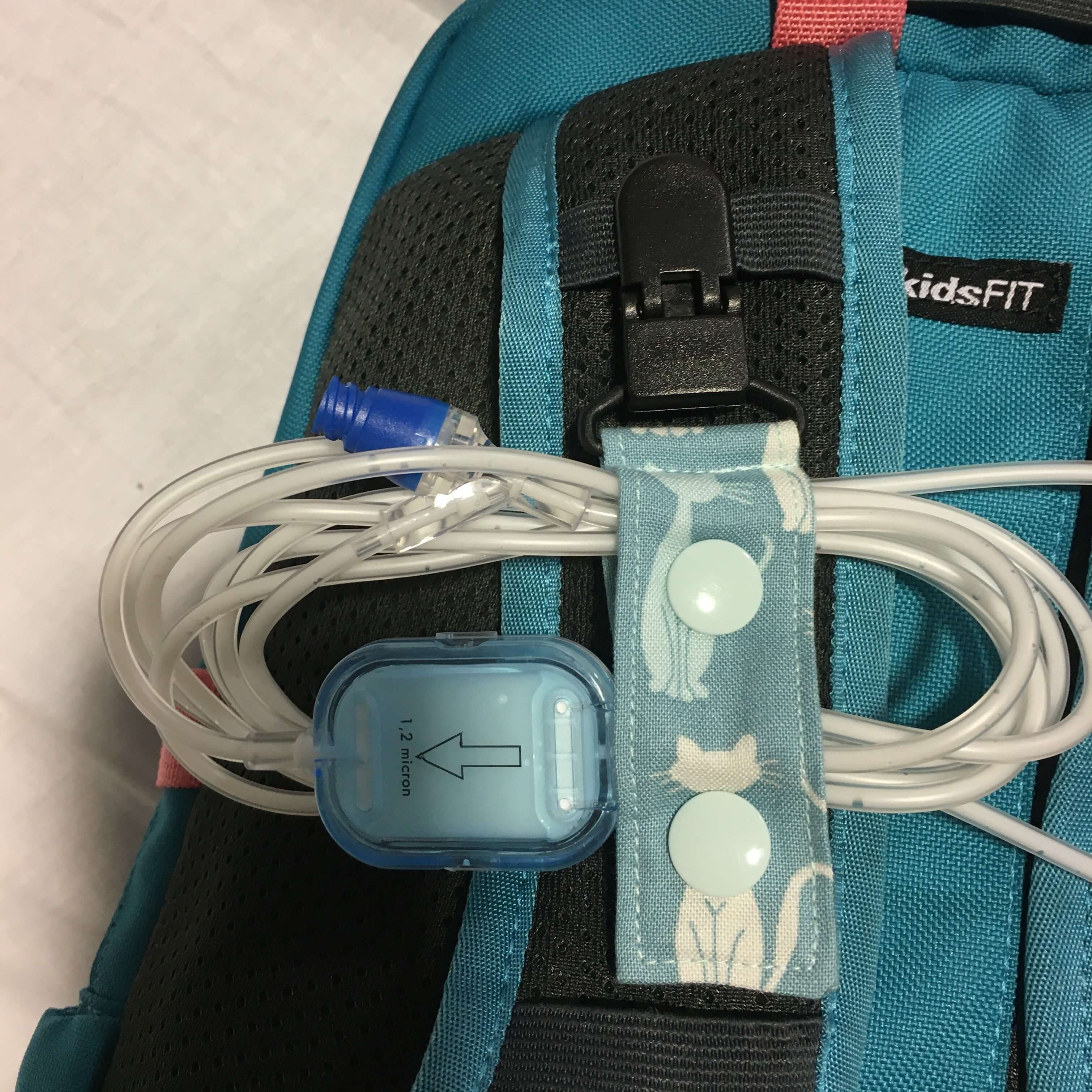 Teal backpack with tubing clip holding cables on a white background